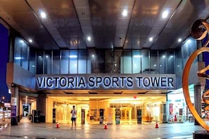 The exterior of Victoria Sports Tower with a prominent entrance and a large glass facade. - Victoria Sports Tower - Cozy Ambiance Condo Unit (Quezon City)