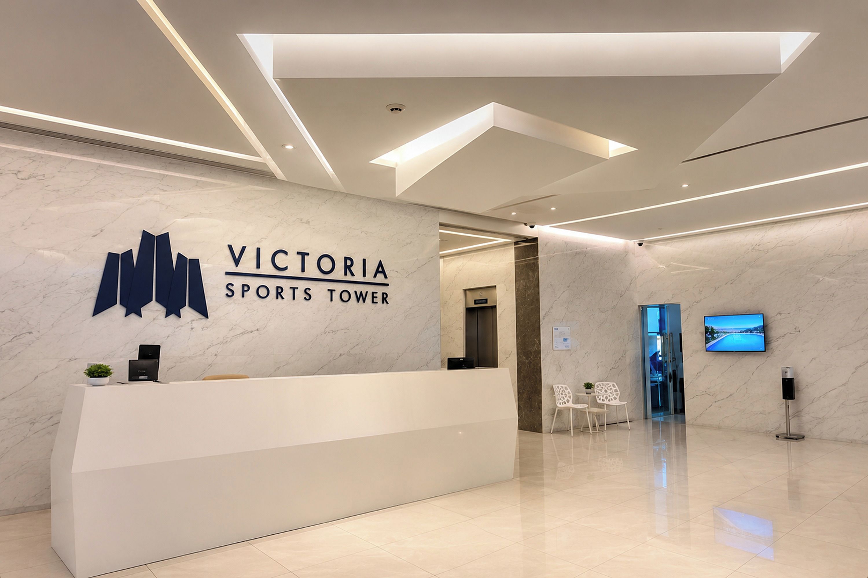 A reception area with a marble wall, a reception desk, a digital screen, and a modern ceiling design.