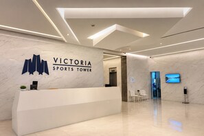 A reception area with a marble wall, a reception desk, a digital screen, and a modern ceiling design. - Victoria Sports Tower - Cozy Ambiance Condo Unit (Quezon City)