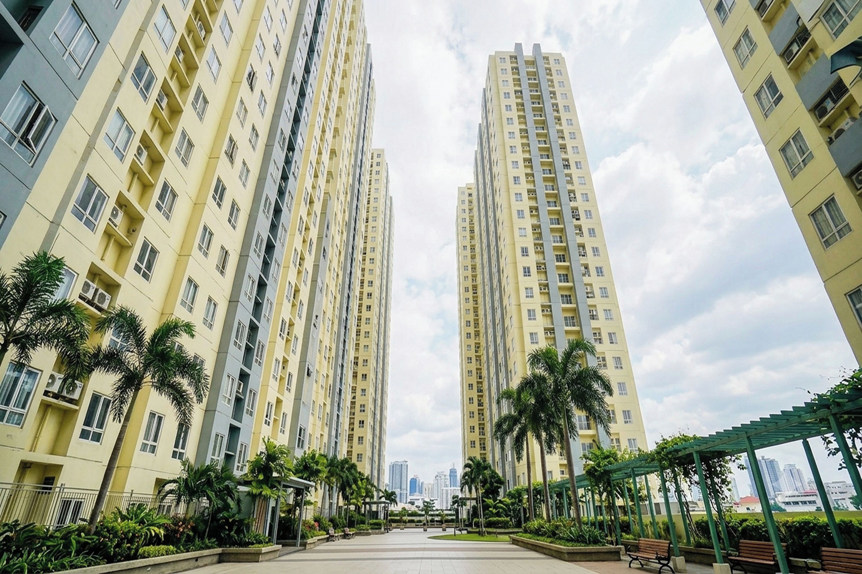 A high-rise residential building with multiple balconies, surrounded by greenery and a clear sky.