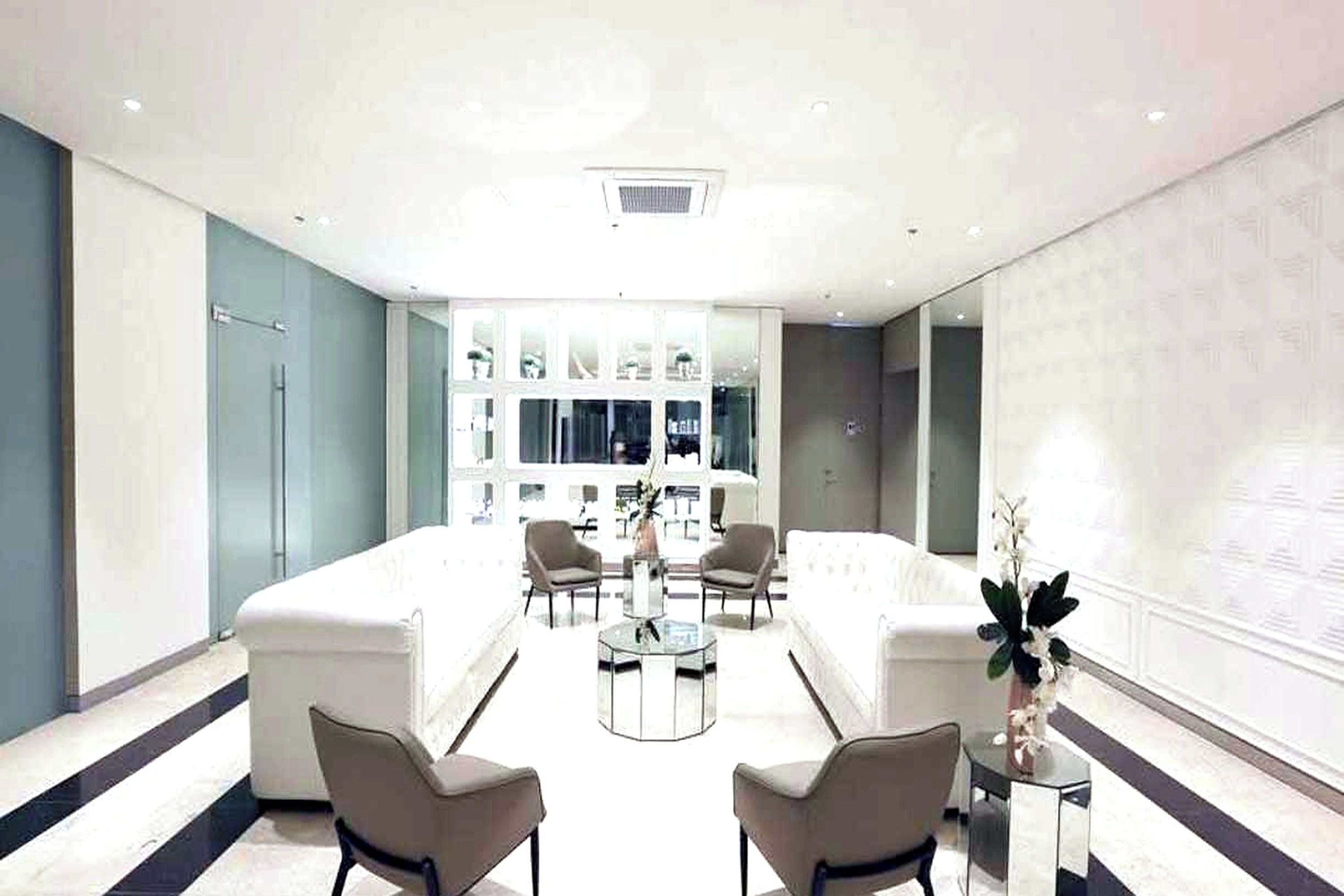 Un moderno vestíbulo de hotel con zona de estar, un mostrador de recepción y un gran ventanal con vistas al interior.