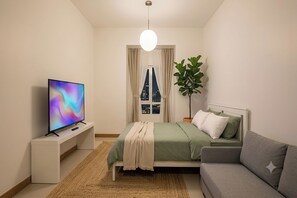 A modern bedroom with a bed, a sofa, a TV, and a plant. - Victoria Sports Tower - Cozy Ambiance Condo Unit (Quezon City)
