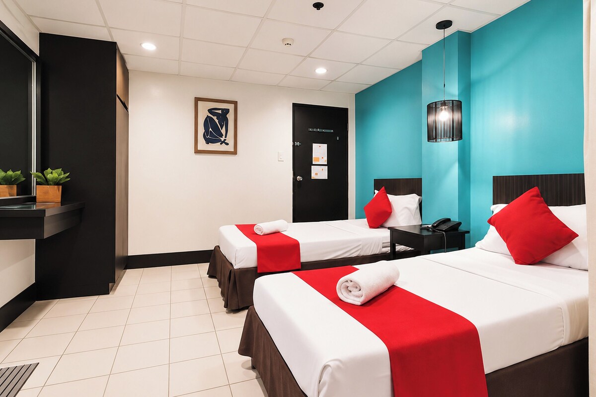 A hotel room with two beds, a desk, a phone, and a wall-mounted light fixture.