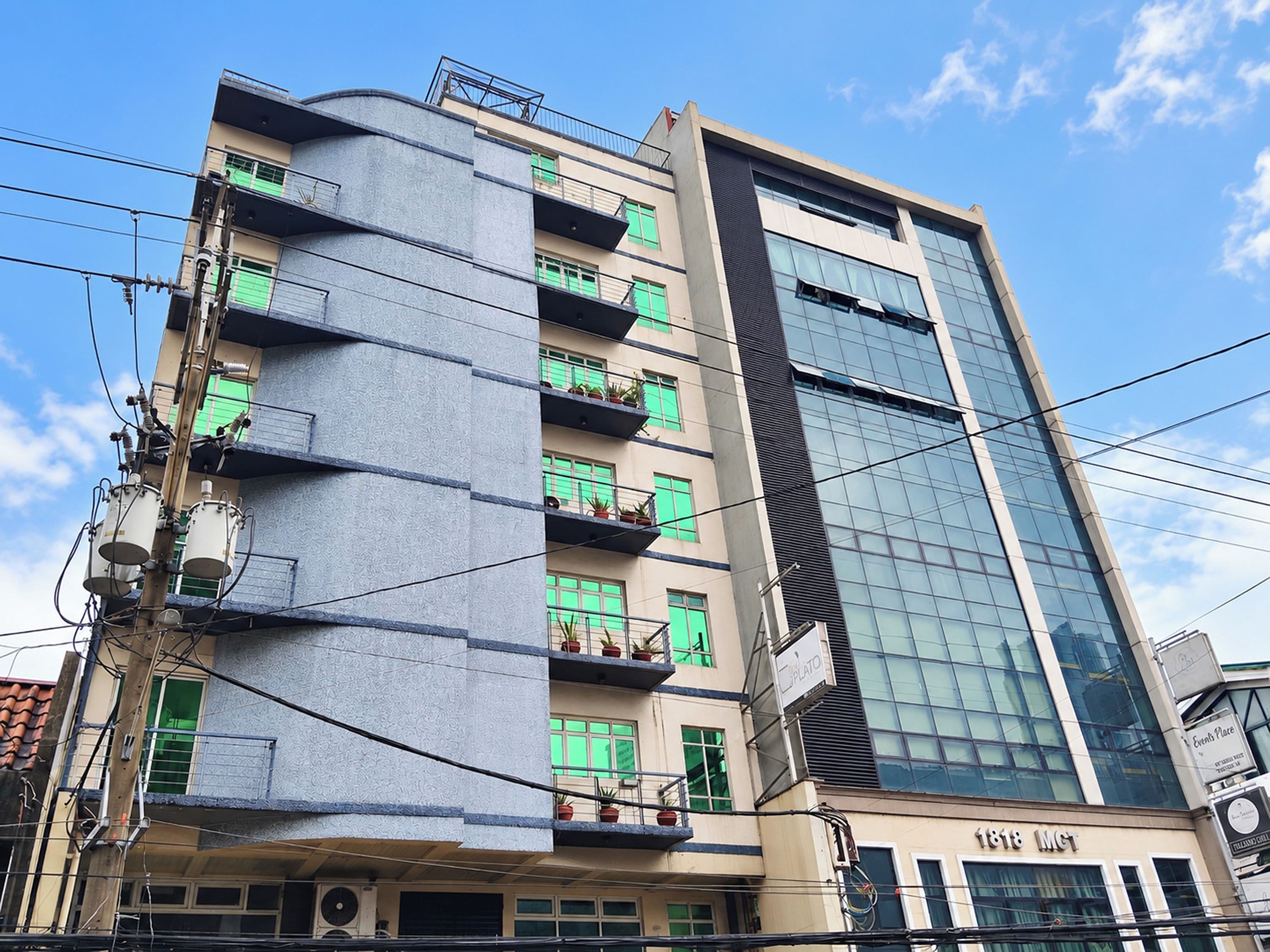 Un edificio de varios pisos con diseño moderno, con balcones adornados con plantas en macetas y un cartel que indica un restaurante.