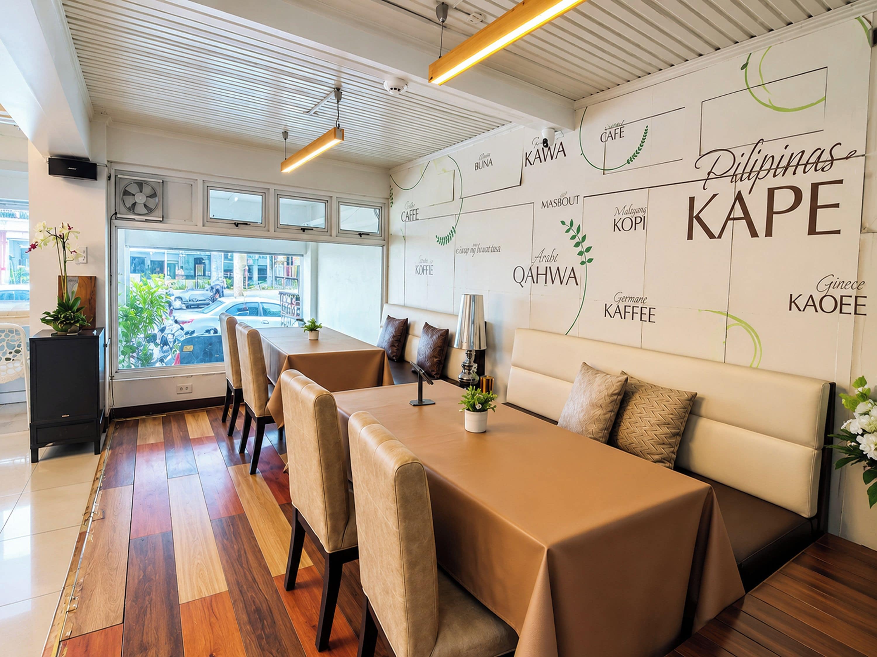 Interior moderno de café com uma mesa comprida, assentos acolchoados e uma parede exibindo diferentes nomes de café.