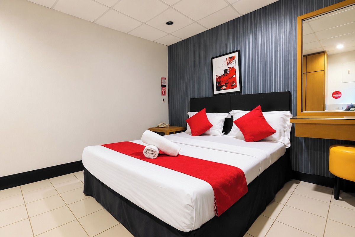 A hotel room with a bed, a nightstand, a mirror, and a red and white bedspread.