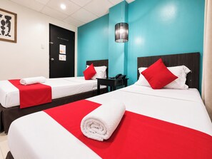 A hotel room with two beds, each with a red and white bedspread, a black nightstand, a desk, and a hanging lamp. - Orange Nest Hotel (Manila)