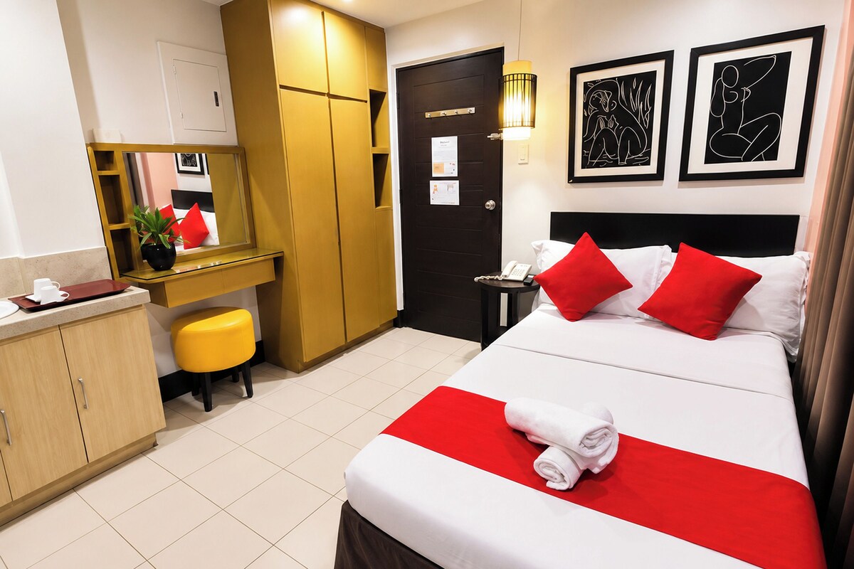 A hotel room with a bed, a desk, a chair, a wardrobe, and a door.