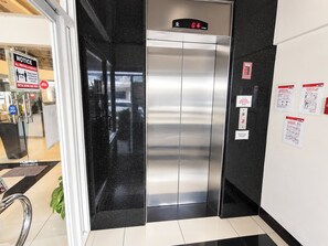 Un ascensor con pantalla digital, un cartel de aviso e instrucciones de emergencia en la pared.