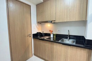 Una cocina compacta con armarios de madera, encimera negra, pileta de acero inoxidable y extractor.