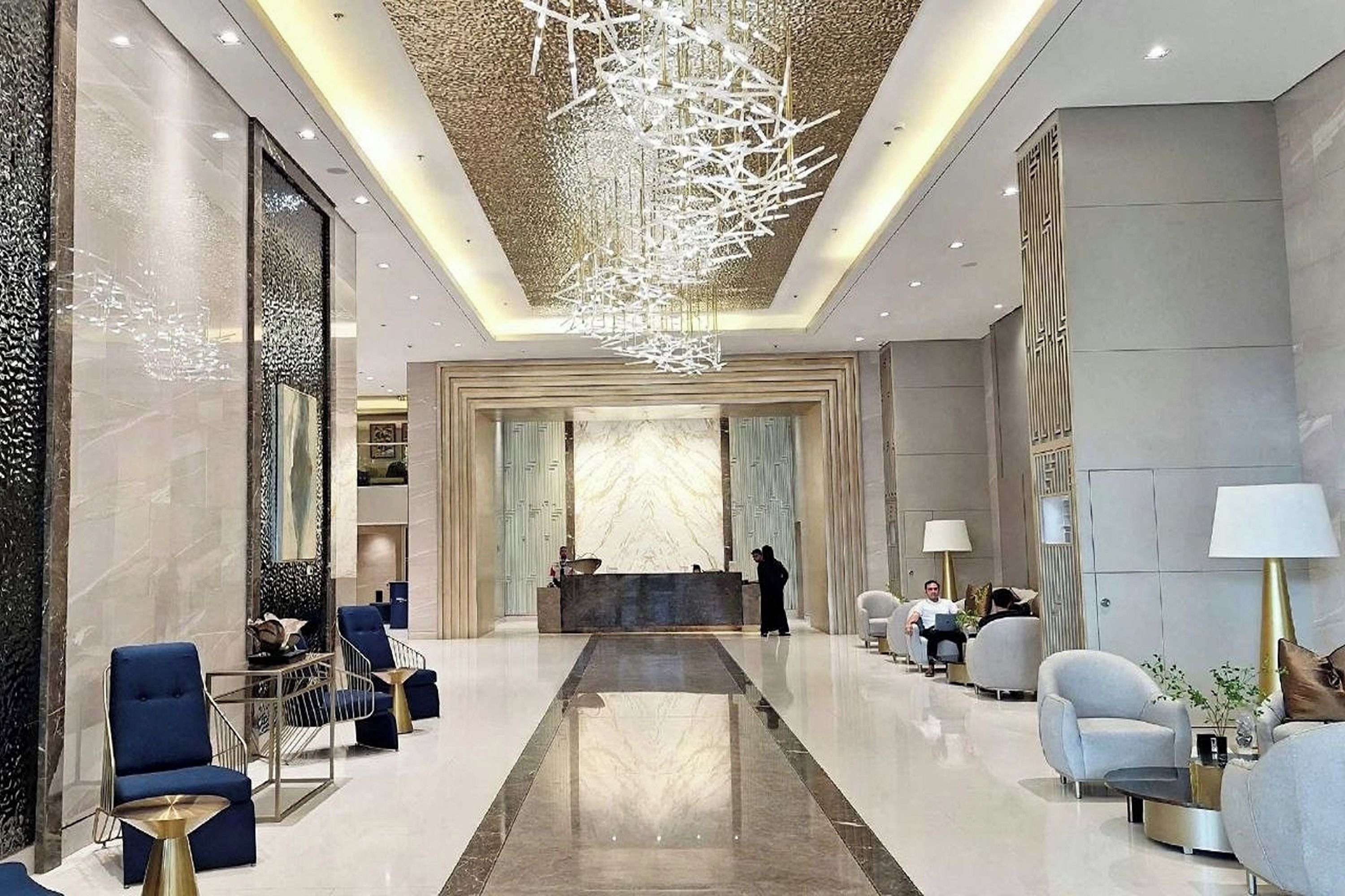 A modern lobby with a central reception desk, seating areas, and a decorative ceiling light fixture.