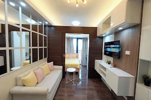 Una habitación de hotel moderna con sofá, televisor, una mesita y cama con cortinas.