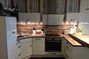 A compact kitchen with white cabinetry, a wooden backsplash, and a built-in oven. - 7 in the house Dune 1 (Cuxhaven\/Duhnen)
