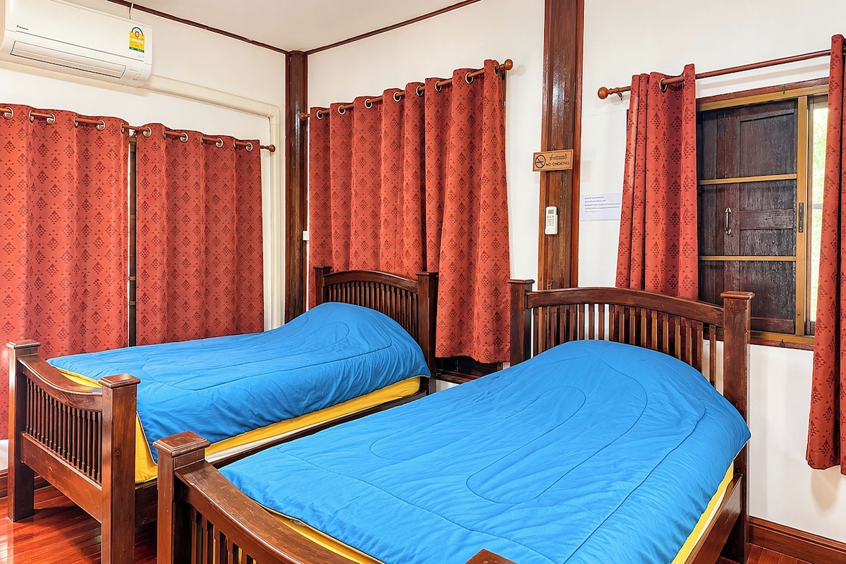 A room with two wooden beds, red patterned curtains, and a wooden wardrobe.