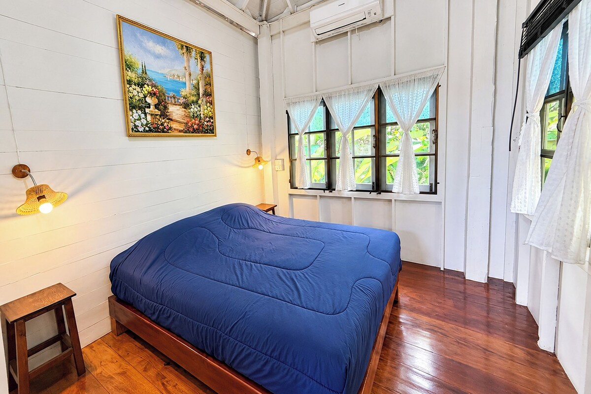 A bedroom with a wooden bed, a painting on the wall, and a window with curtains.