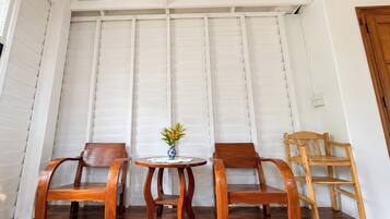 Una habitación con dos sillas de madera, una mesita con un florero y una silla de madera apoyada en una pared blanca con paneles.