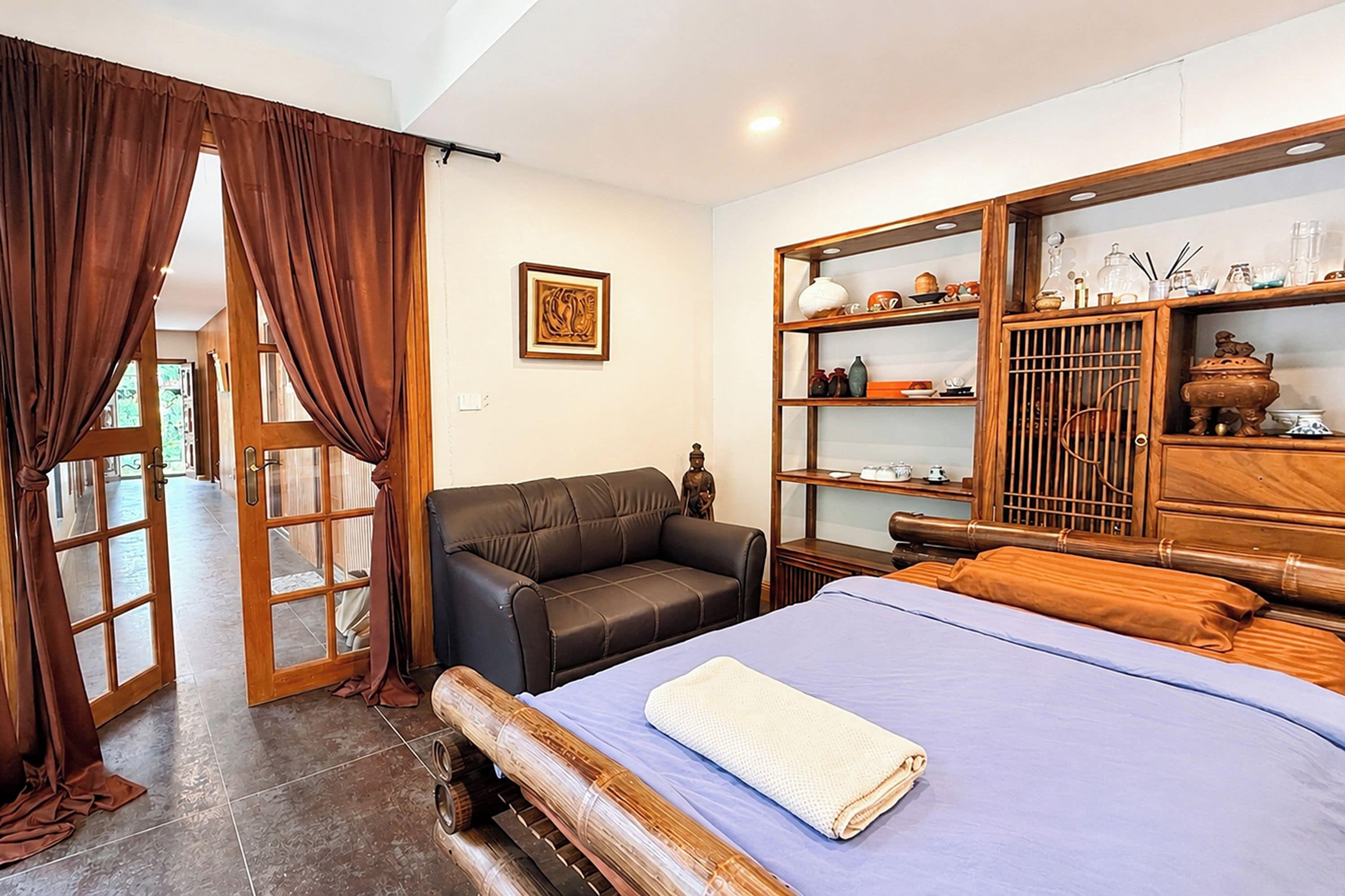 Un dormitorio con cama, sofá, armario de madera y adornos, y una puerta con cortinas.