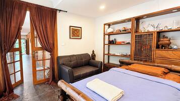 Un dormitorio con cama, sofá, armario de madera y adornos, y una puerta con cortinas.