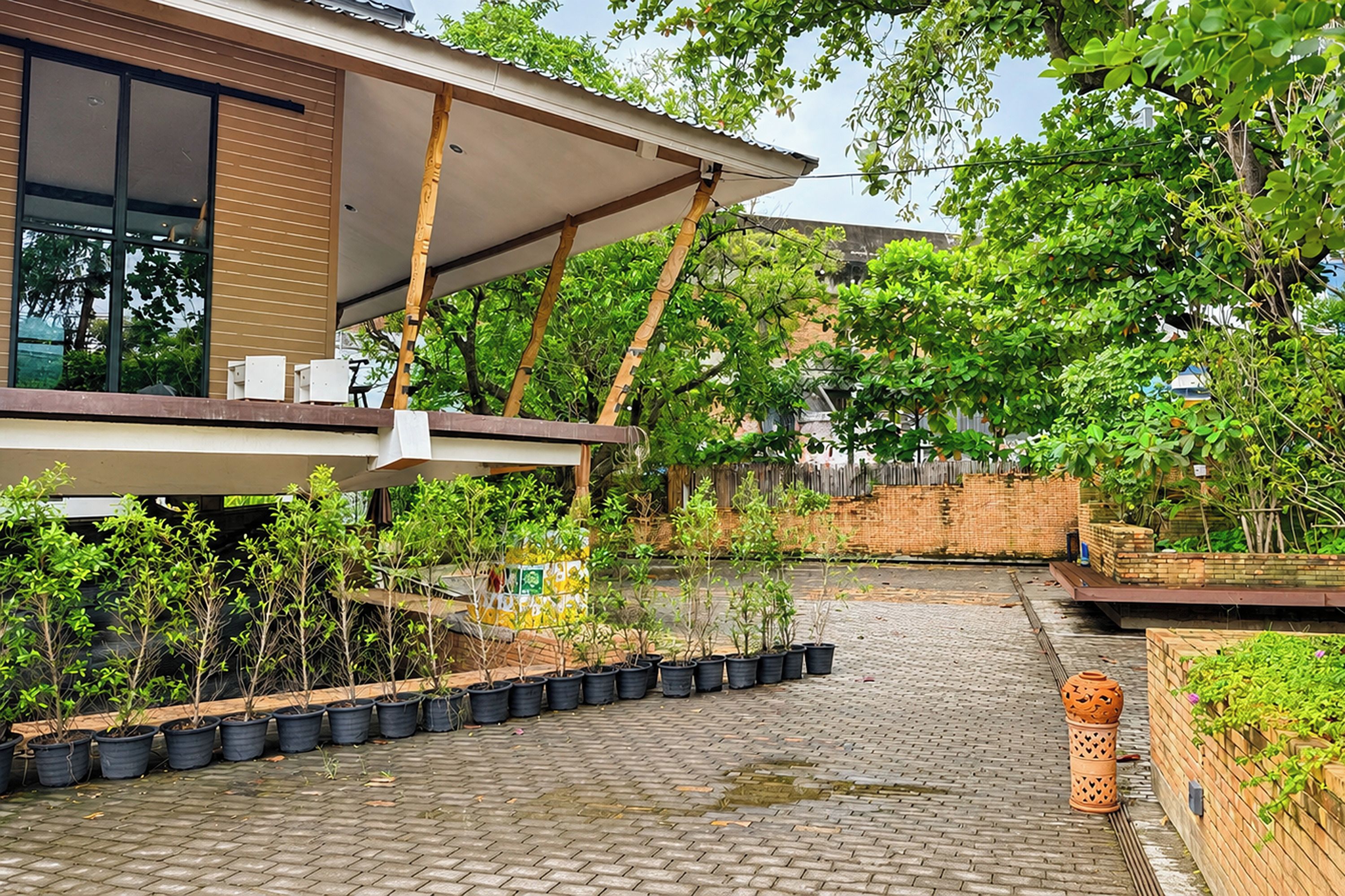 A modern building with a covered outdoor area, potted plants, and a brick pathway.