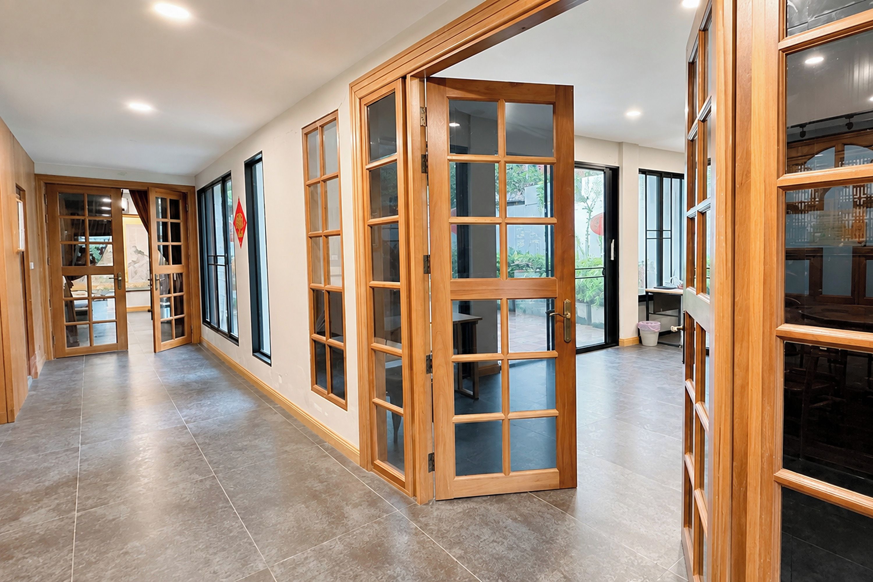 A corridor with wooden doors and windows, leading to a dining area with a table and chairs.