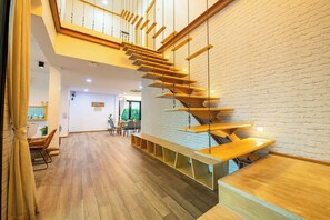 Un interior moderno con una escalera de madera, una zona de comedor y una pared de ladrillo blanco.