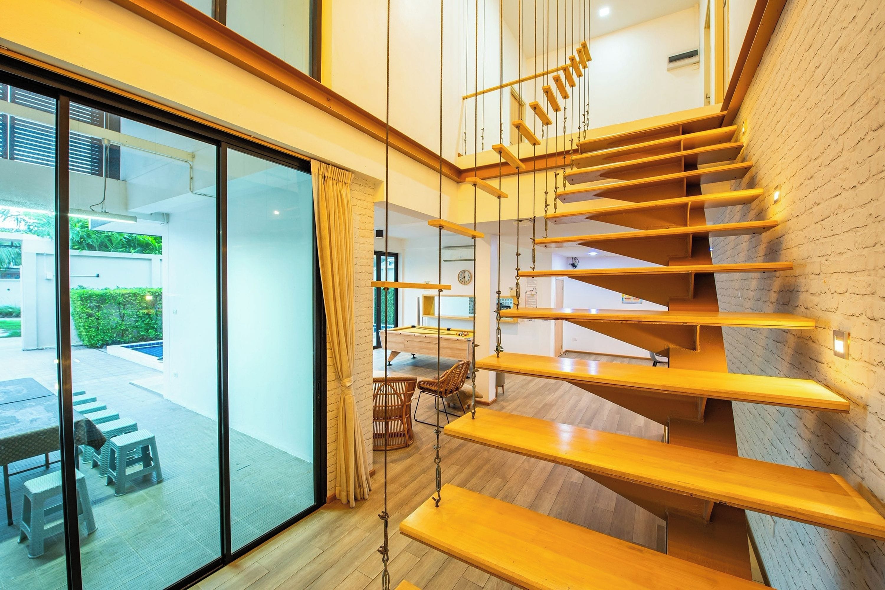 Un interior moderno con una escalera de madera, una mesa de billar y una puerta de cristal que da a un espacio exterior.