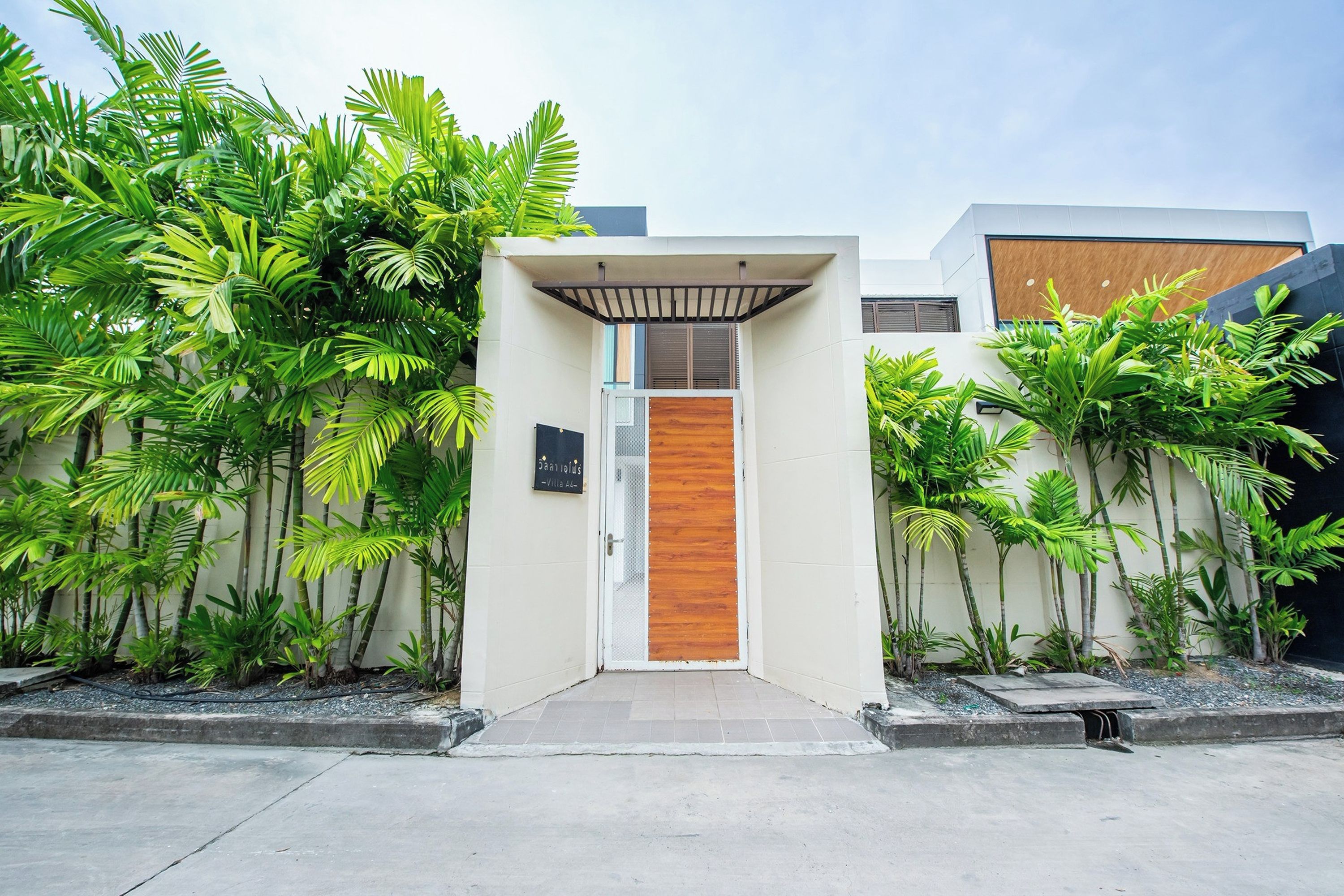 A modern building entrance with a wooden door, surrounded by lush tropical plants.