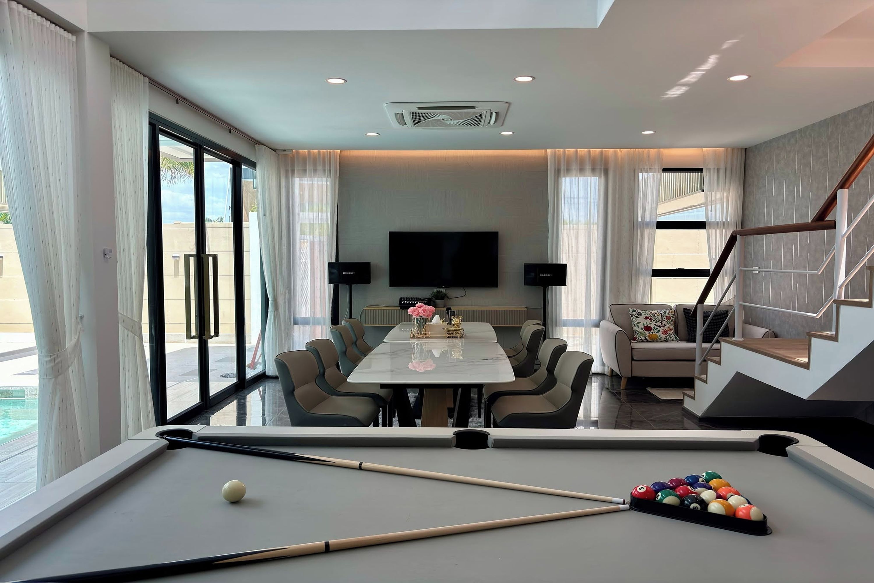 A modern living room with a pool table, a dining area, and a staircase.