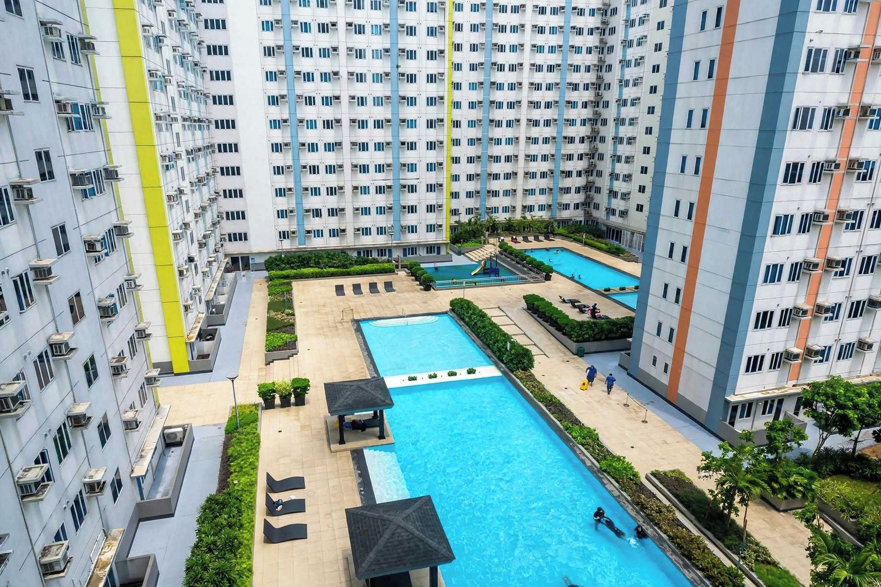 A high-rise residential building with multiple balconies, a central swimming pool, and a smaller pool area.