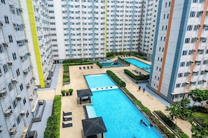 A high-rise residential building with multiple balconies, a central swimming pool, and a smaller pool area. - Mplace Cozy Hotel (Quezon City)