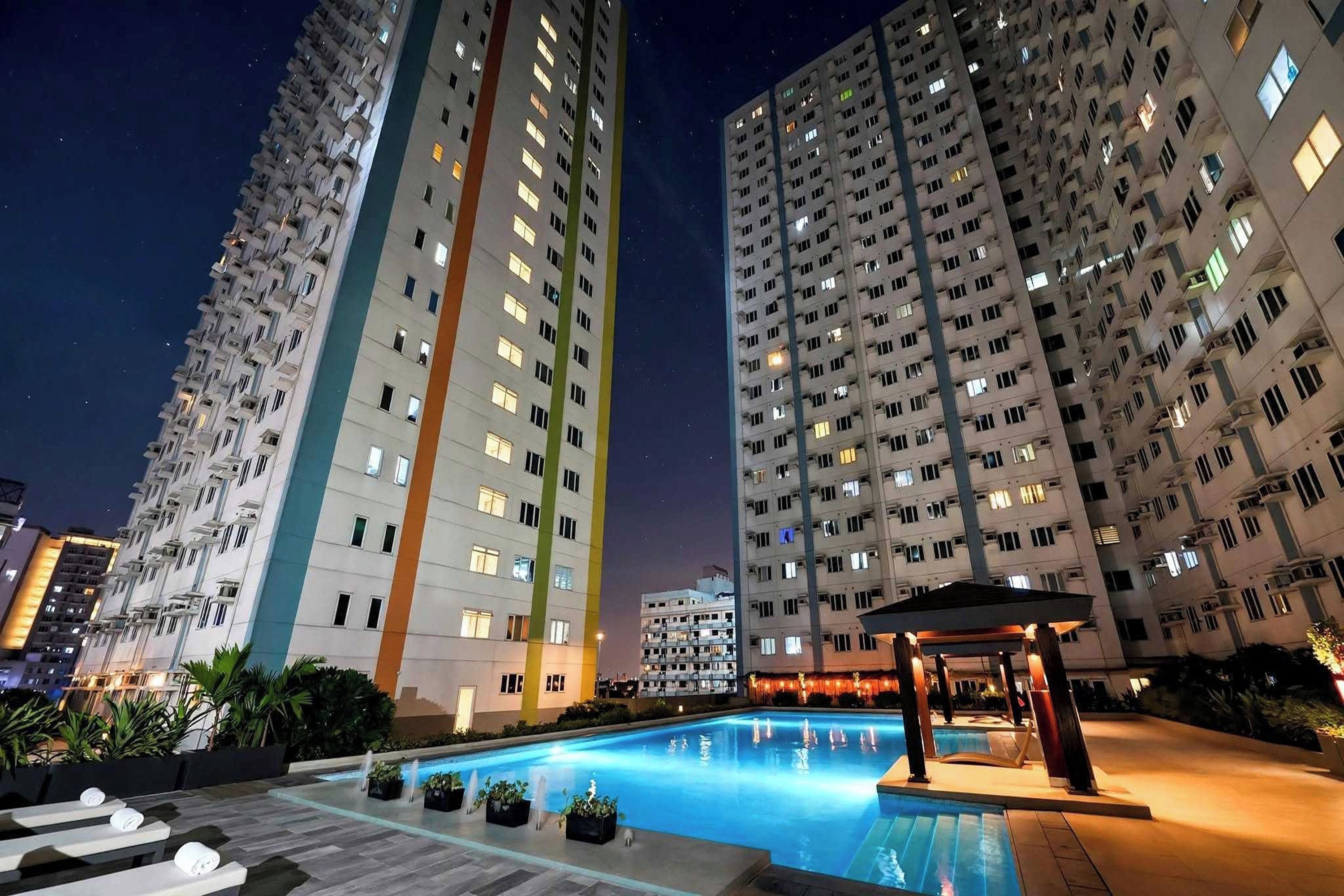 A nighttime view of a high-rise residential building with a pool and lounge area.