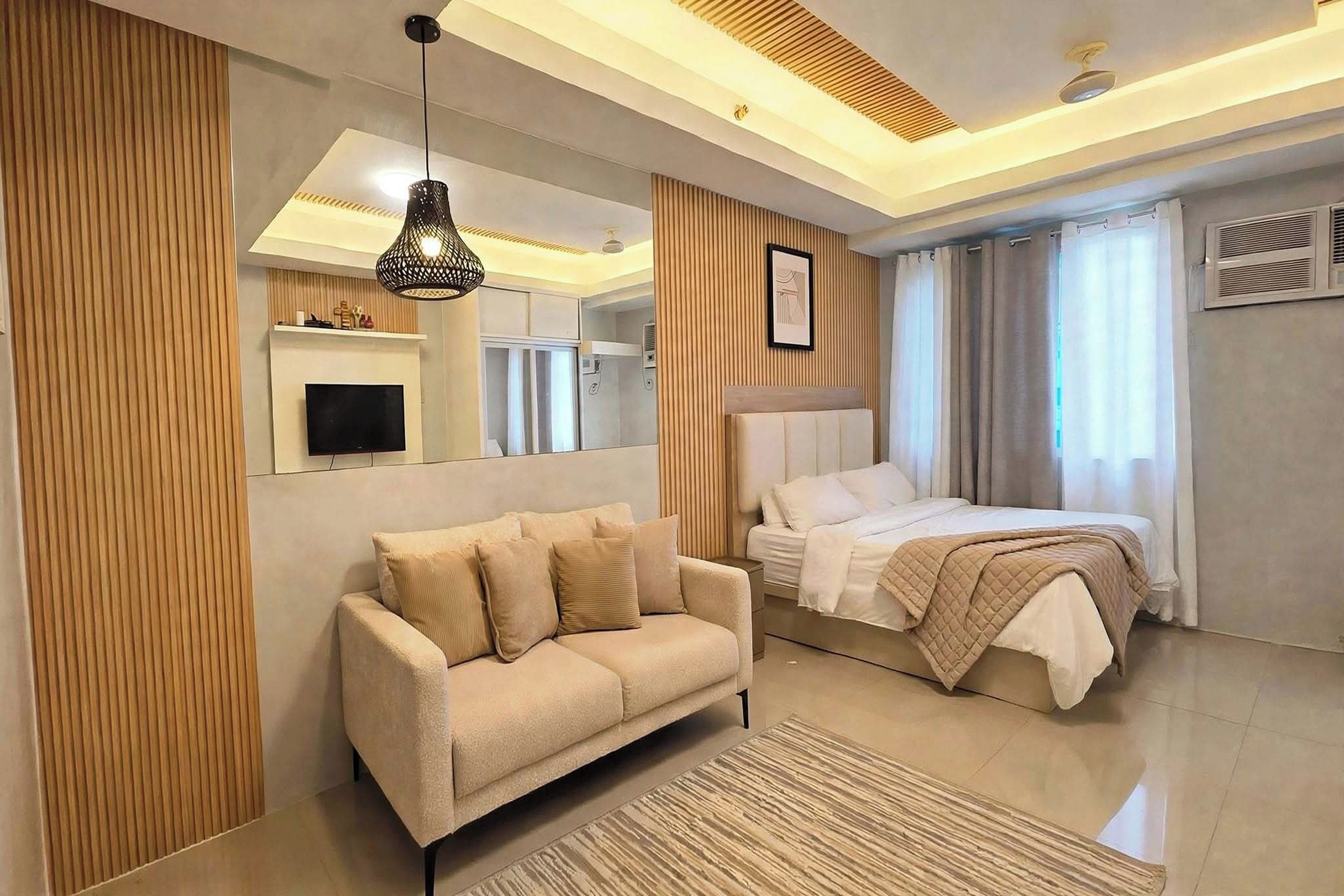 A modern bedroom with a sofa, a bed, a mounted TV, and a ceiling light fixture.