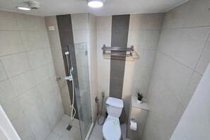 A modern bathroom with a glass shower enclosure, a toilet, and a small potted plant. - Mplace Cozy Hotel (Quezon City)