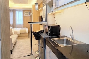 A compact kitchenette with a microwave, sink, and a small dining area with a chair. - Mplace Cozy Hotel (Quezon City)