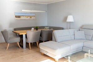 A modern living room with a grey sofa, a wooden dining table, and grey armchairs. - House Panorama WHG 33 (Cuxhaven)