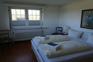 A bedroom with a double bed, a chair, a nightstand, a lamp, and a window. - Friesenhaus Carl Jensen Holiday Apartment 1 (Wenningstedt-Braderup)