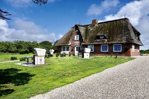 A traditional thatched-roof house with a gravel driveway and a grassy lawn. - Friesenhaus Carl Jensen Holiday Apartment 1 (Wenningstedt-Braderup)