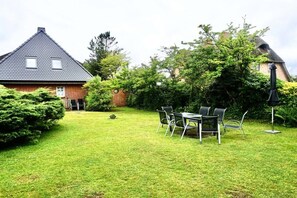 A house with a sloped roof, a brick exterior, and a well-maintained lawn. There is a table with chairs in the yard. - Holiday apartment with 4 bedrooms (Wenningstedt-Braderup)
