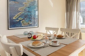 Un coin repas avec une table en bois, des chaises blanches, une carte encadrée au mur et des aliments pour le petit-déjeuner disposés sur la table.