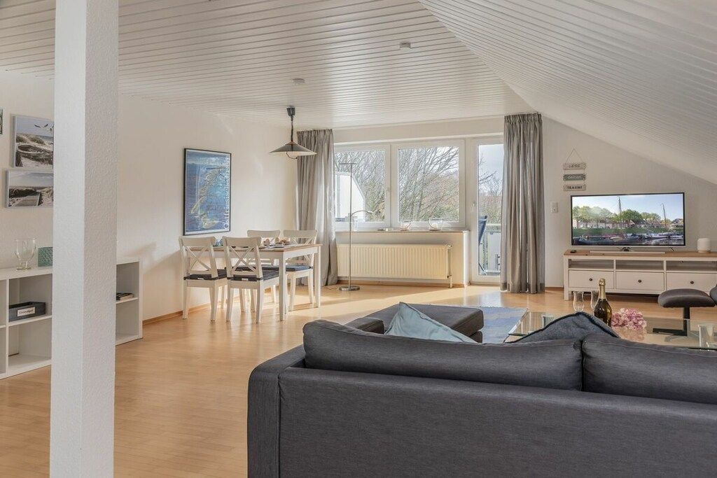 Una sala moderna con un sofá, una mesa de comedor, sillas y un televisor.