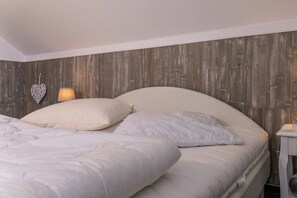 A bedroom with a wooden headboard, two beds with white bedding, a bedside lamp, and a heart-shaped decoration on the wall. - 50006 House Deichkieker (Harlesiel)