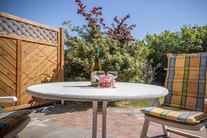 A round table with a bottle and glasses, a wooden fence, and a chair with a patterned cushion. - 50006 House Deichkieker (Harlesiel)