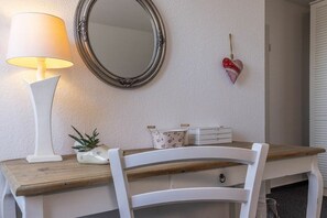 A room with a wooden desk, a white chair, a lamp, a mirror, a small plant, and a heart-shaped decoration. - 50006 House Deichkieker (Harlesiel)