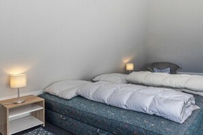 A bedroom with two beds, each with a pillow and a bedside lamp. There is a wooden nightstand with a lamp on it. - 50006 House Deichkieker (Harlesiel)