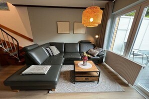 Ein modernes Wohnzimmer mit einer Eckcouch, einem Couchtisch mit einer Vase und einem großen Fenster mit Jalousien.