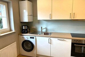 Eine kleine Küche mit Waschmaschine, Kaffeemaschine, Spüle und Backofen.