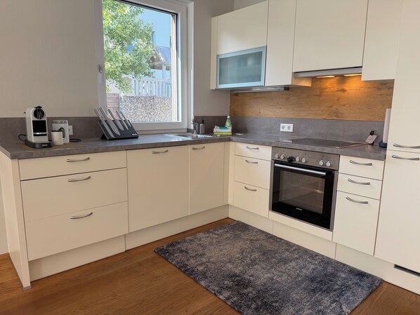 A modern kitchen with white cabinets, a built-in oven, and a window overlooking a backyard.