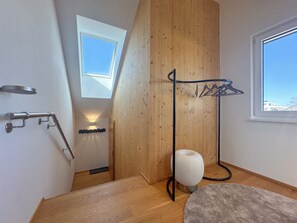 A modern interior with a wooden floor, a white chair, a coat rack, and a skylight.