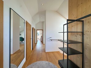 Un pasillo con suelo de madera, alfombra gris y un estante metálico negro.