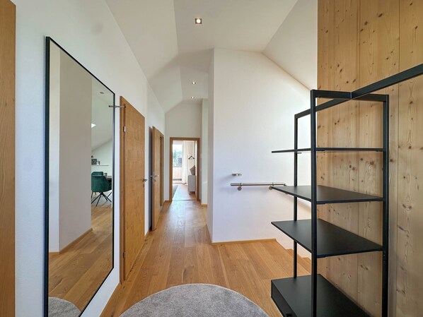 A hallway with wooden flooring, a grey rug, and a black metal shelf unit.
